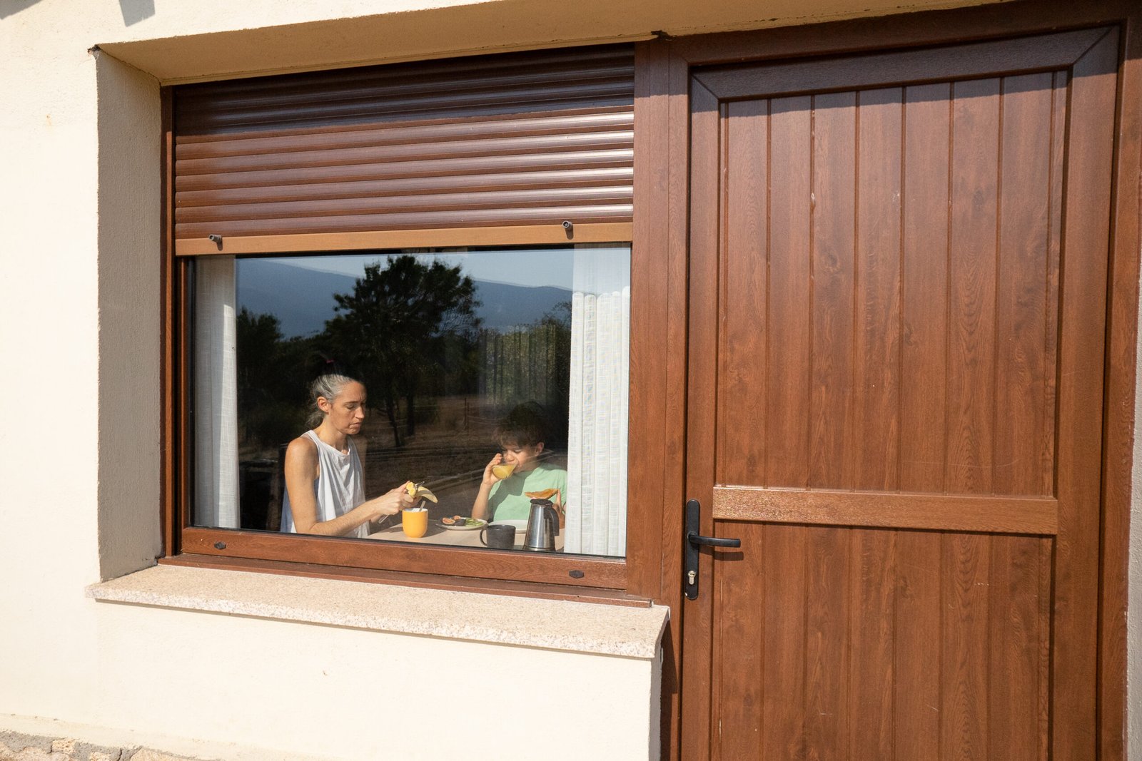Mutter und Kind frühstücken am Fenster mit teilweise geöffnetem Rollladen